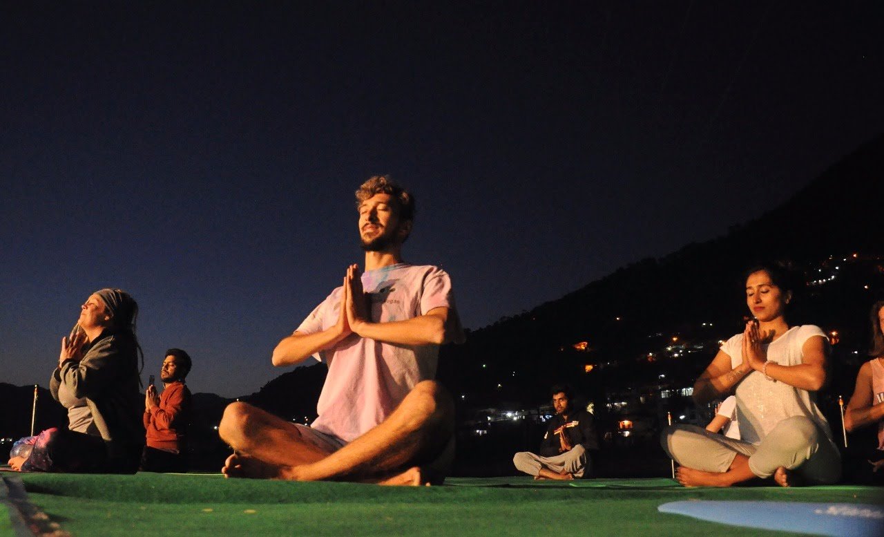 Students meditate as a group at dusk while the lights of the Uttarkashi valley glow below, during a Yoga Bhawna Mission session.